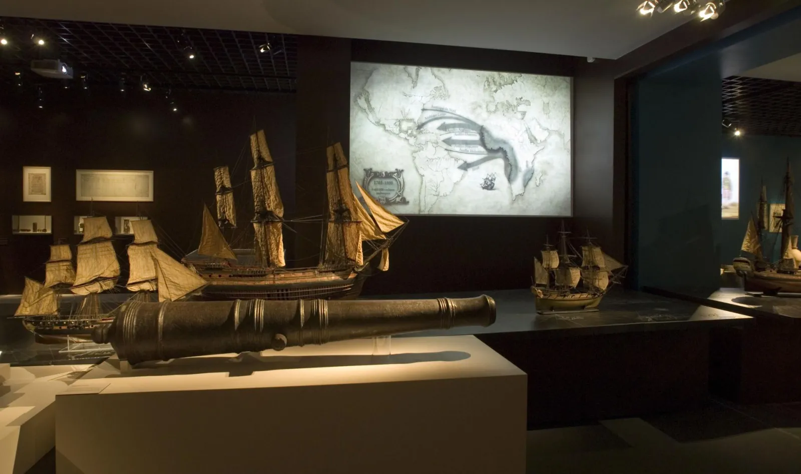 Museum display at Musée d'Aquitaine in Bordeaux featuring golden ship models, a bronze cannon, and a historical map projection, showcasing Bordeaux's maritime and commercial heritage