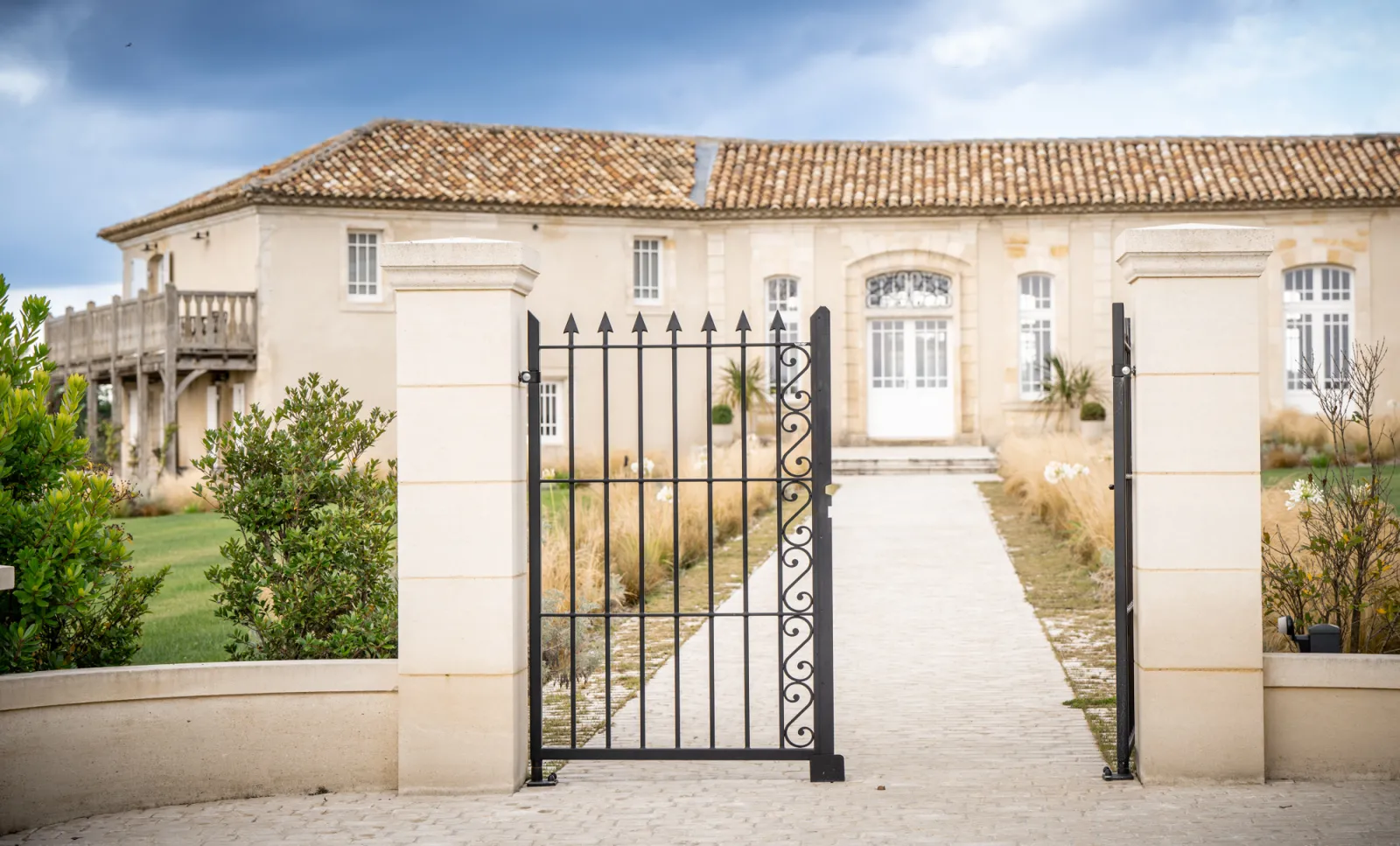 Black wrought iron gate opening onto the driveway of a classical stone manor house, Château La Garde in Bordeaux