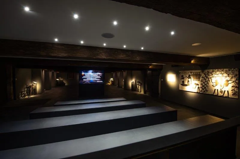Modern museum interior at Château de Portets in Bordeaux featuring illuminated staircase steps, exhibition display cases with artifacts, and digital screens in a dark, elegant atmosphere.