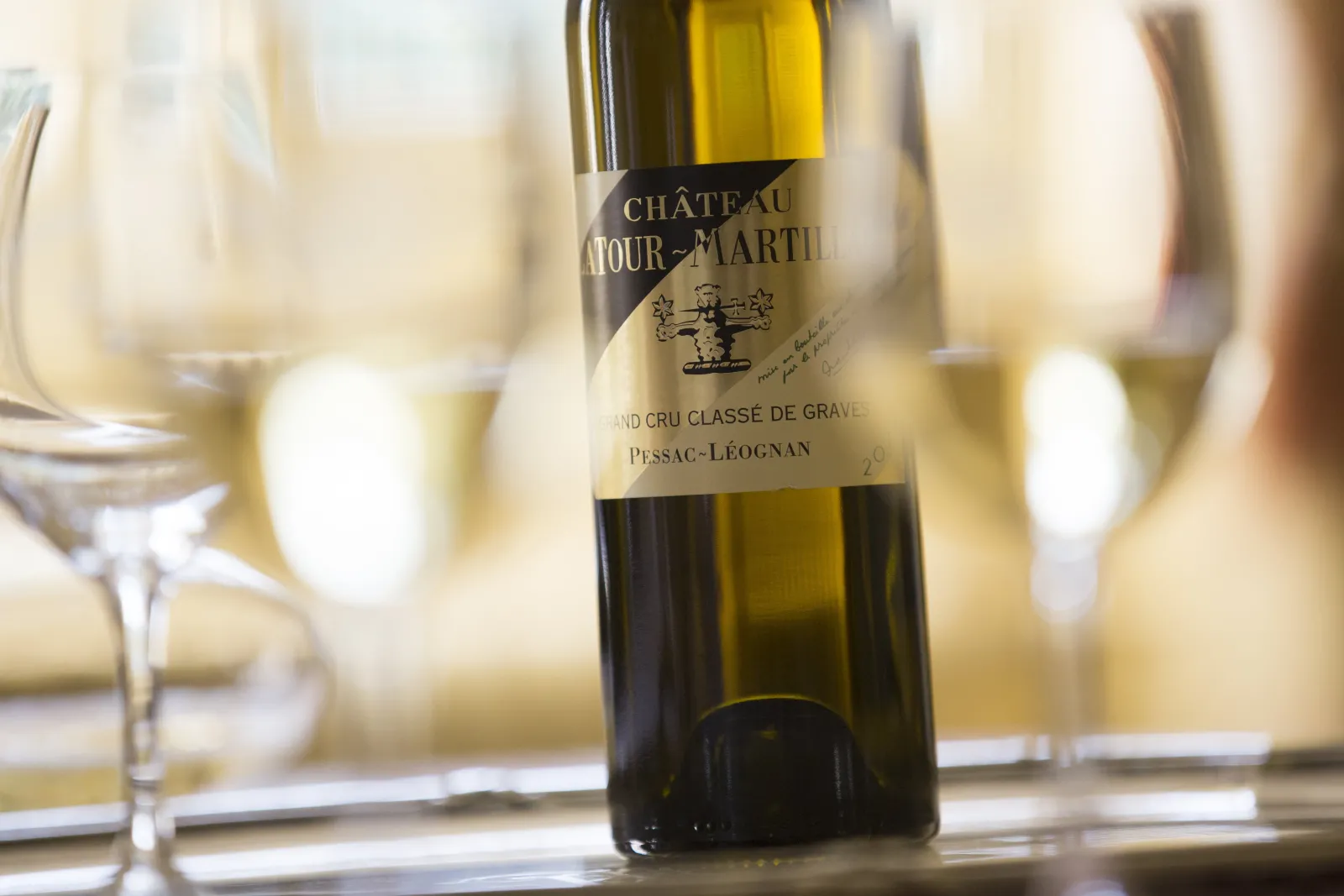 Bottle of Château Latour-Martillac, Grand Cru Classé de Graves from Pessac-Léognan, surrounded by glasses of white wine at table.