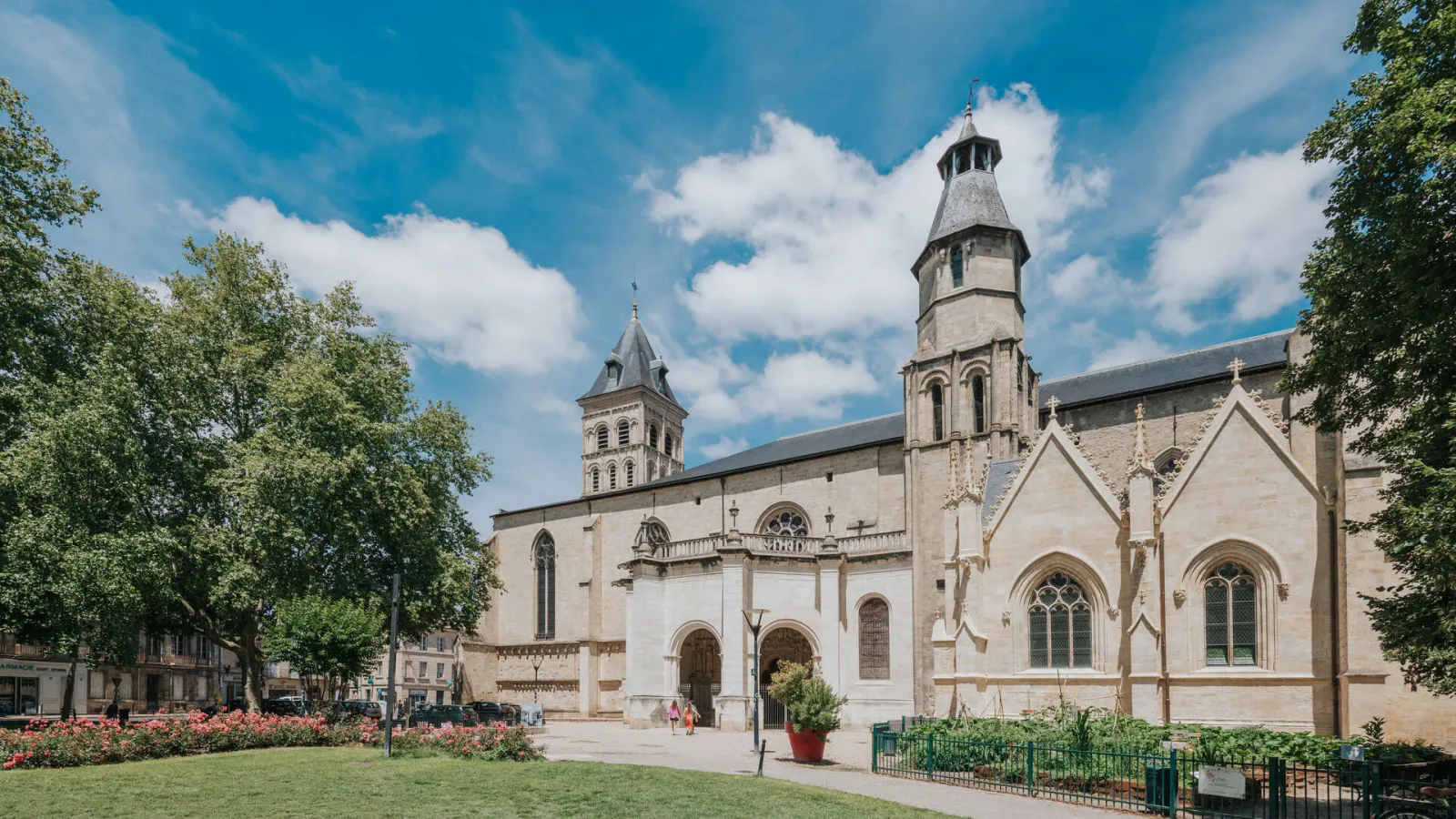 Basilica of Saint-Seurin in Bordeaux, a white stone religious building with two towers, surrounded by greenery and a landscaped square under a clear blue sky.
