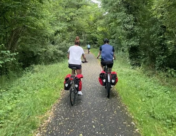 Two cyclists riding bikes on a tree-lined cycling path with other users in the background on a forest trail in Bordeaux.