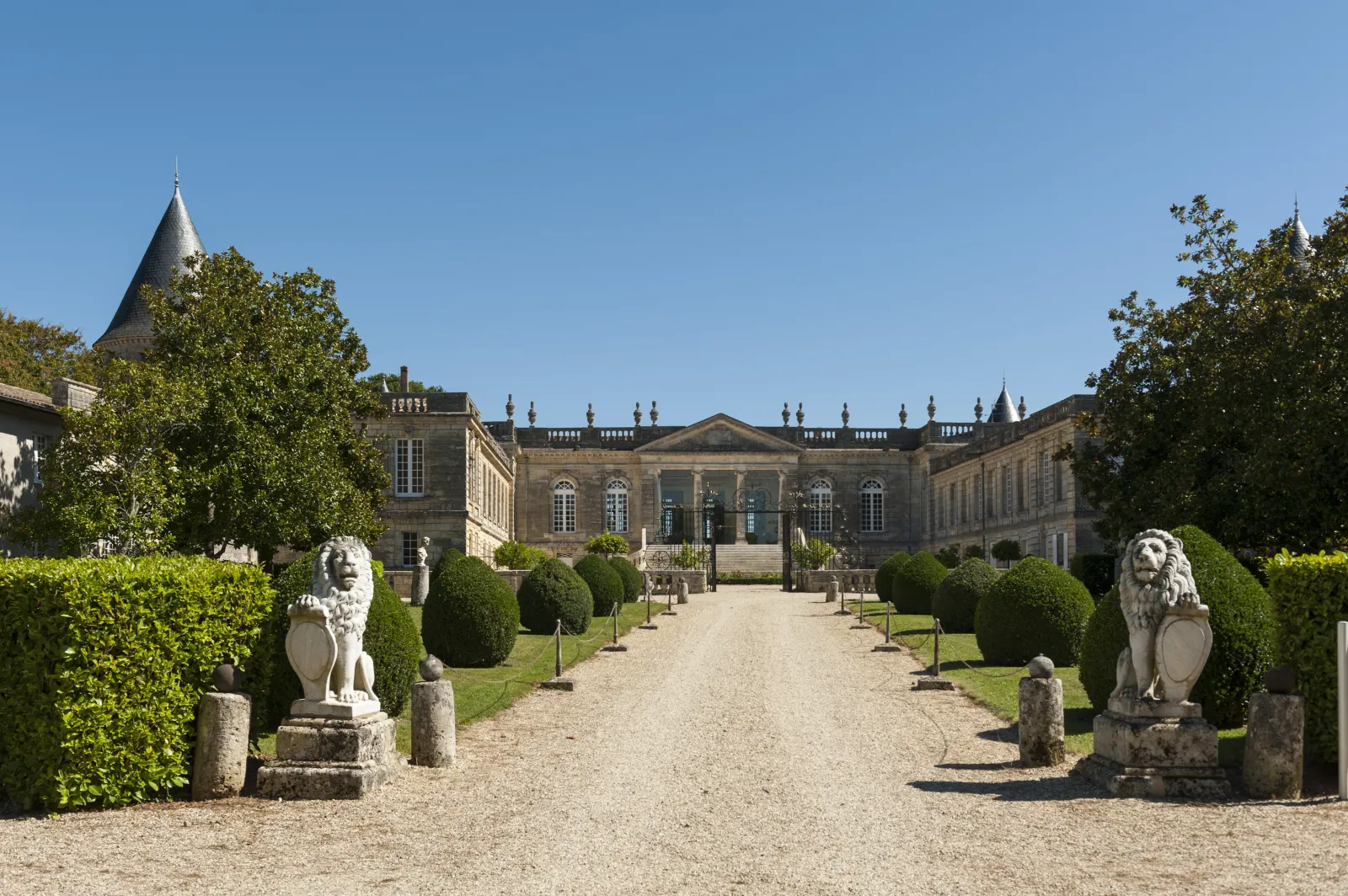 Front view of Château Saint-Georges in Bordeaux featuring a gravel pathway, stone lion statues, trimmed boxwood hedges and classical stone facade