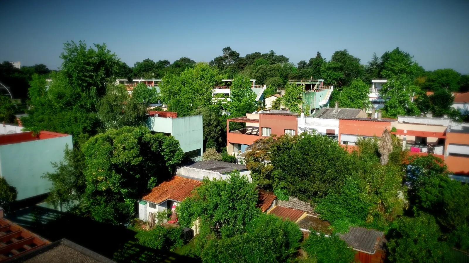 Aerial view of the Cité Frugès in Pessac, a modern residential district designed by Le Corbusier featuring white, red, and green houses surrounded by lush greenery.