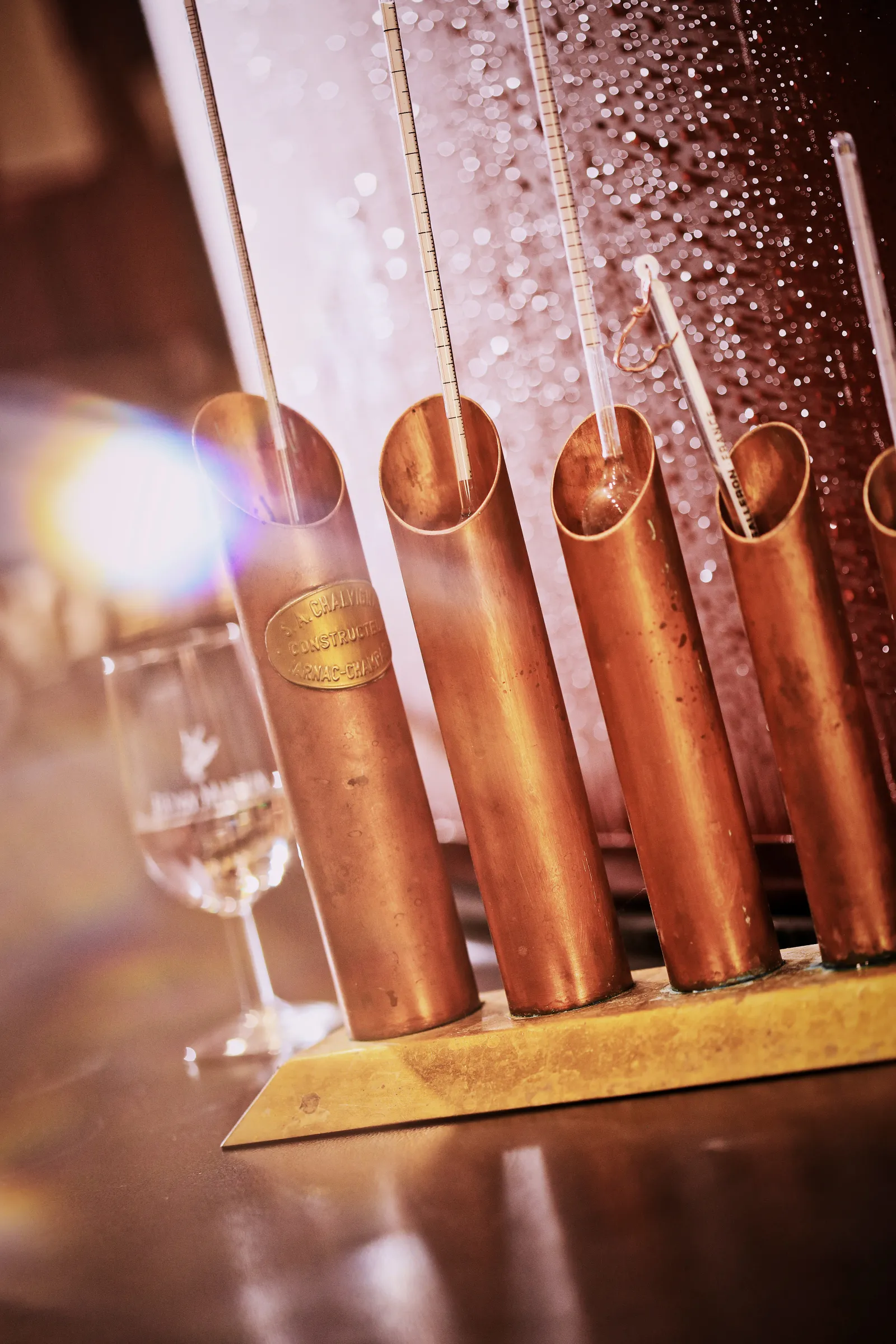 Row of copper-colored Rémy Martin cognac bottles suspended by golden chains against a sparkling pink and gold backdrop, displayed in an elegant tasting setting in Bordeaux.