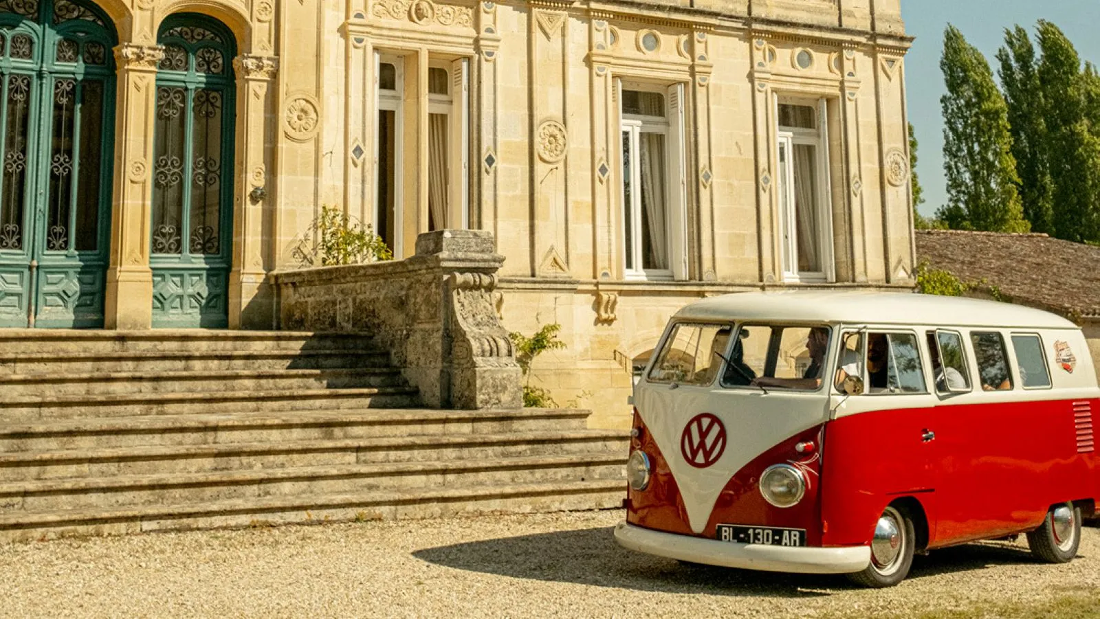 A vintage red and white Volkswagen camper van from the 1950s parked in front of an elegant neoclassical building in Bordeaux, with stone steps and ornate columns.