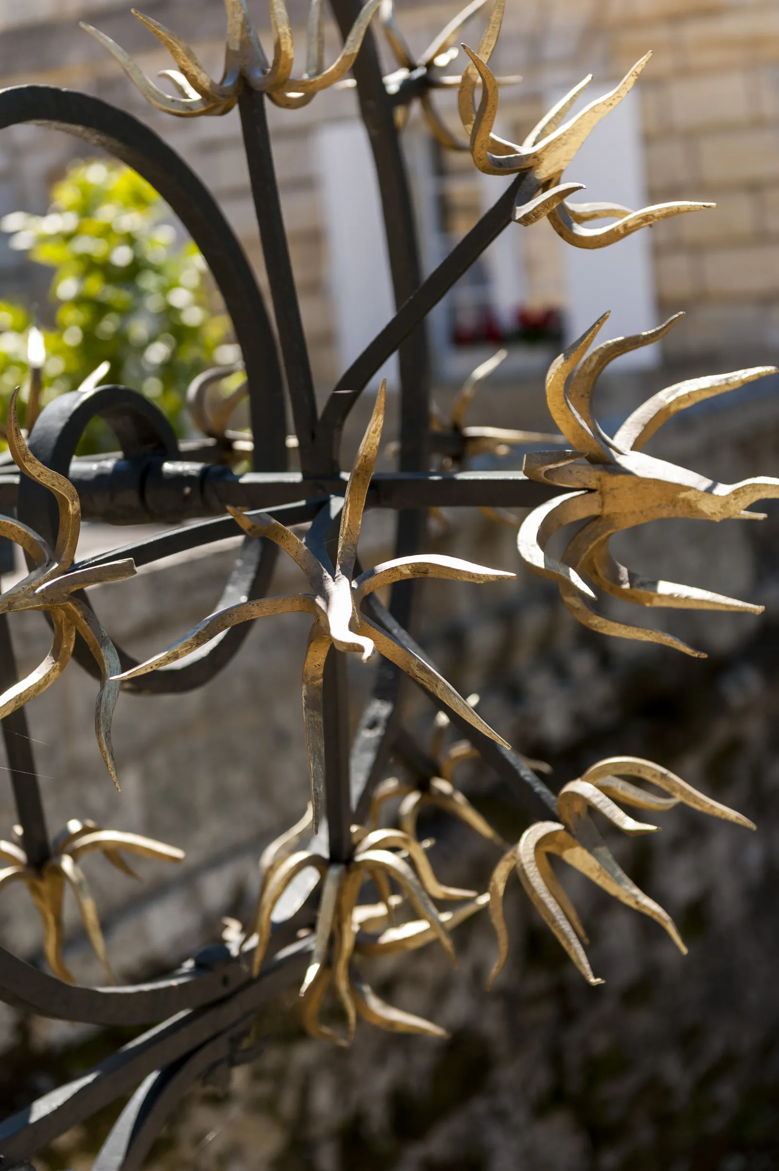 Close-up of golden star-shaped floral decorations on black metal framework, with a blurred garden background at Château Saint-Georges in Bordeaux.
