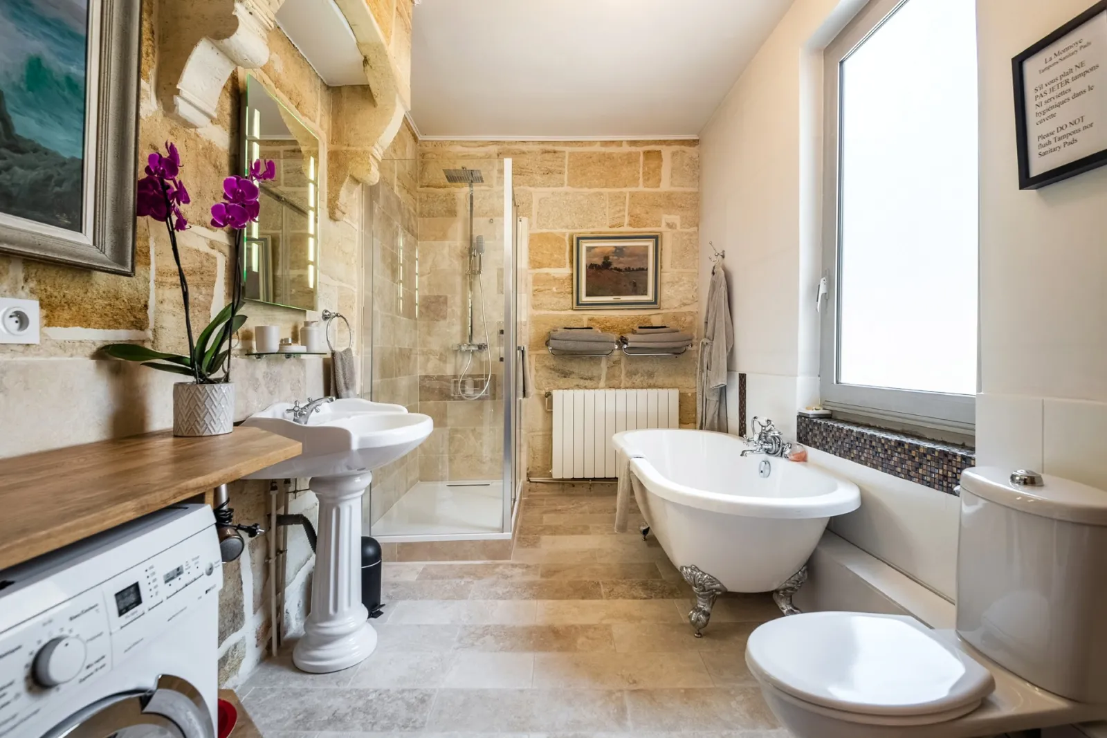 Luxurious bathroom featuring a freestanding bathtub, walk-in shower, stone sinks, light beige tiling and modern fixtures, located in Bordeaux La Monnoye.
