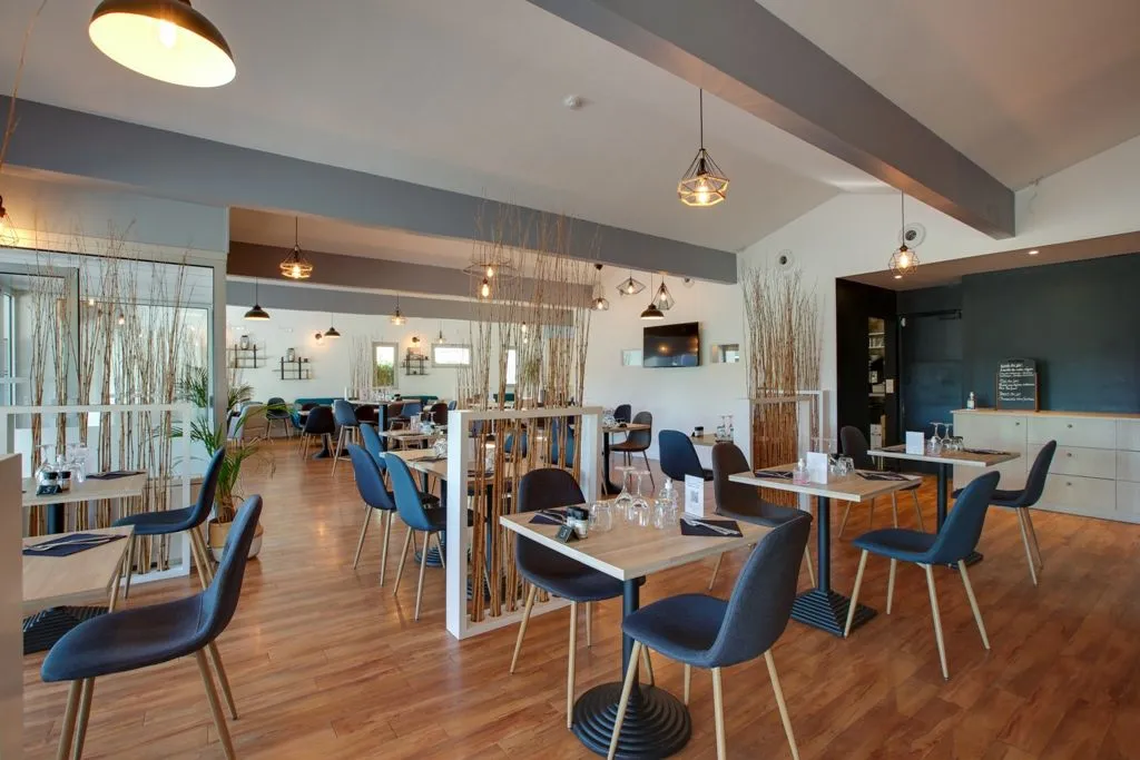 Modern interior of Apolonia restaurant in Bordeaux featuring wooden tables, blue chairs, pendant lighting, and natural fiber room dividers.