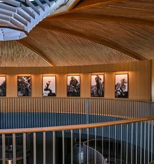 Interior of the Bordeaux Dome featuring a light wood upper gallery with gray metal railing and six framed photographs on the walls beneath a wooden ceiling.