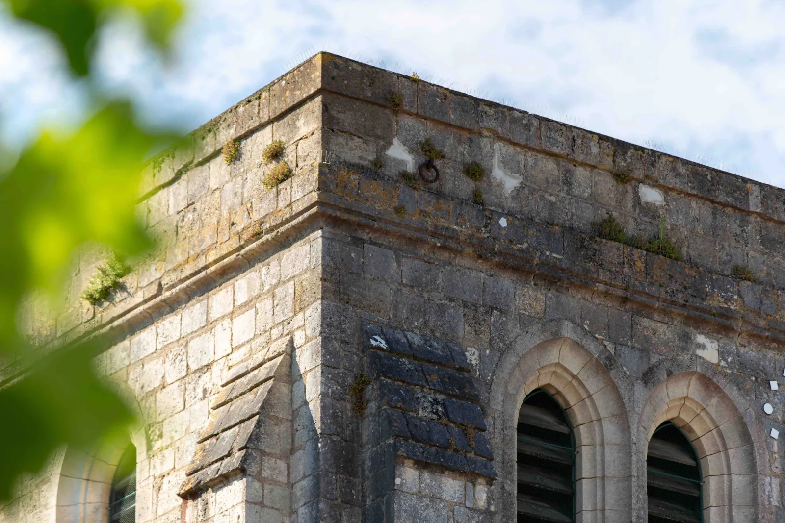 Architectural detail of the Basilica Notre-Dame-de-la-fin-des-Terres in Bordeaux: stone corner with two ogival arch openings, showing age and weathering with moss growth