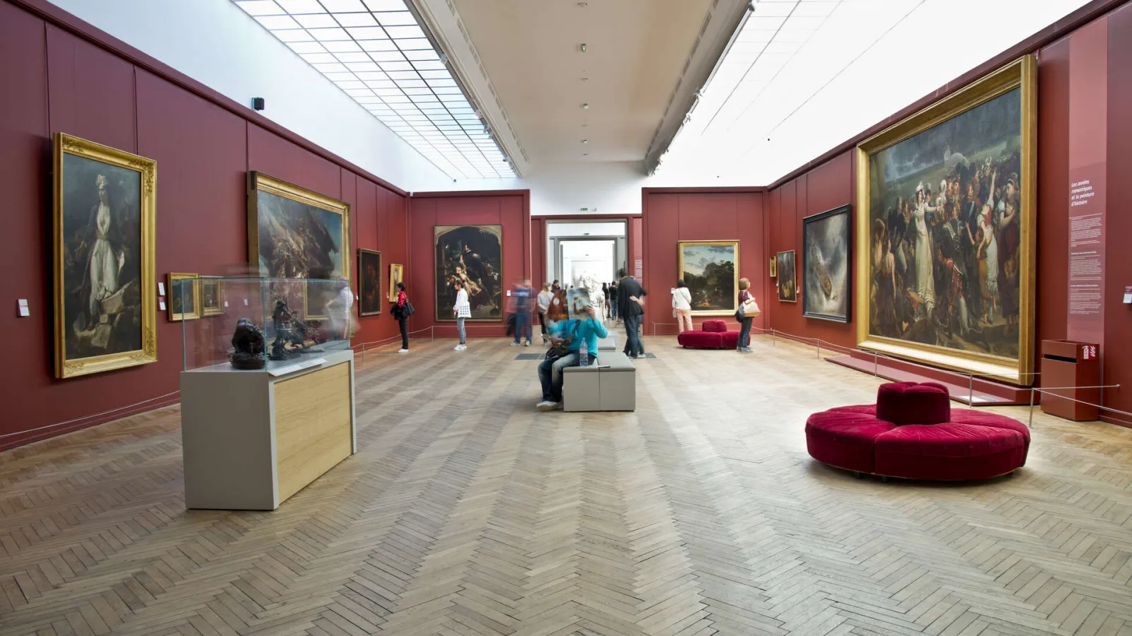 Gallery room at Bordeaux Museum of Fine Arts featuring red walls, old master paintings in gilded frames, red velvet seating, and visitors.