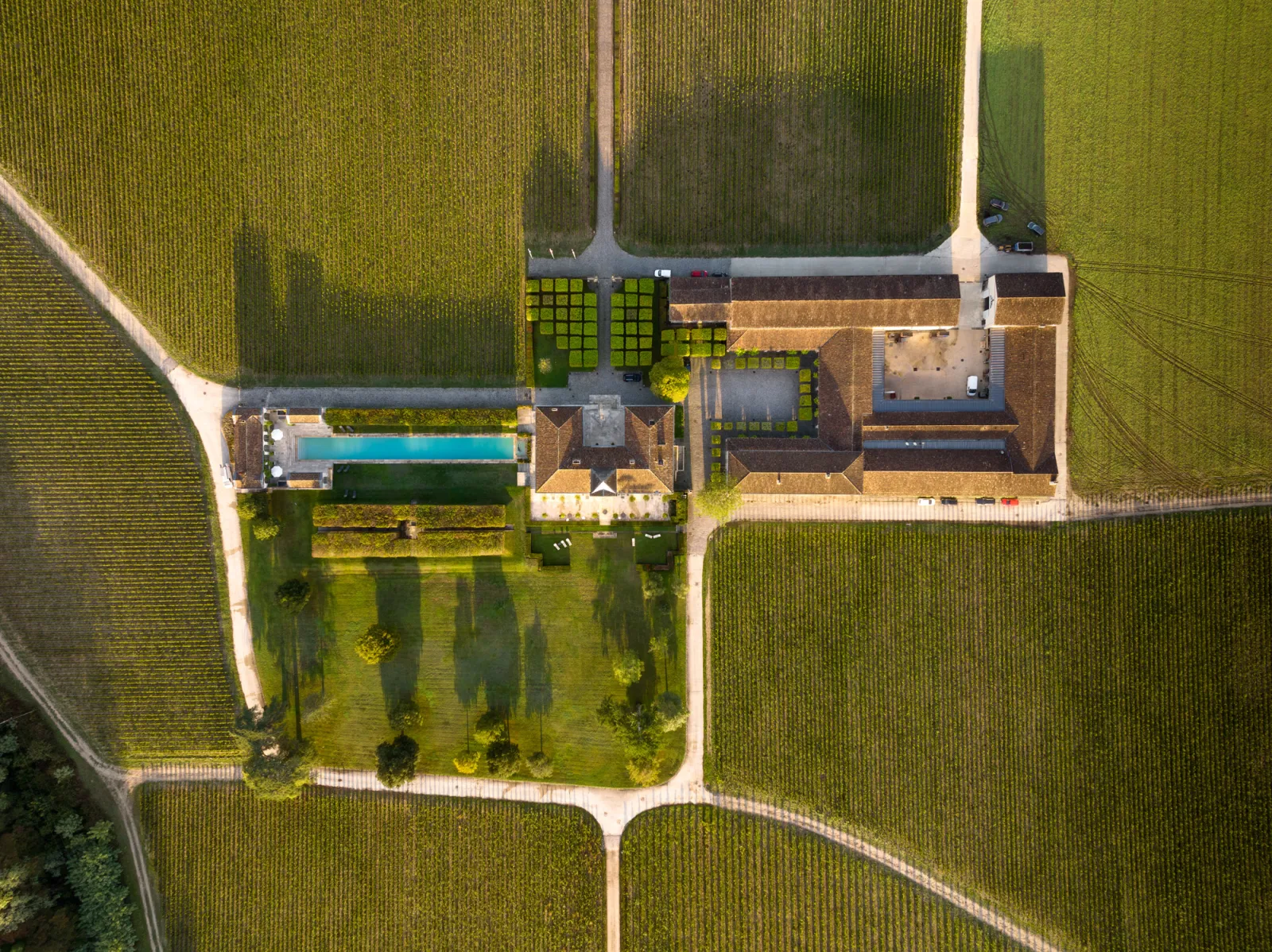 Aerial view of Château du Tertre near Bordeaux showing stone buildings, a blue swimming pool, manicured gardens and surrounding vineyards