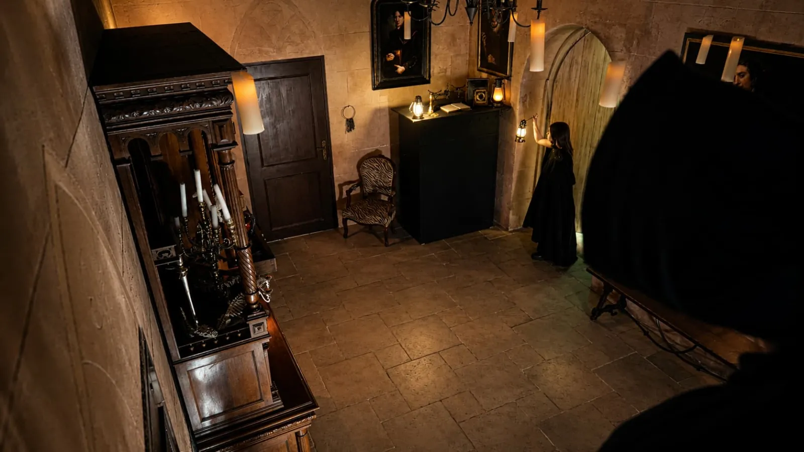 Historic wine cellar in Bordeaux featuring wooden barrels, antique furniture, candelabras and visitors in dark clothing exploring the underground gothic atmosphere.