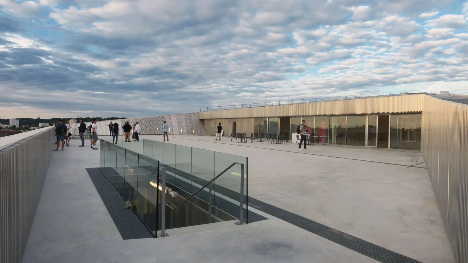 Panoramic terrace of La Méca in Bordeaux with visitors, modern metal and glass building, access stairway, and cityscape view under cloudy sky