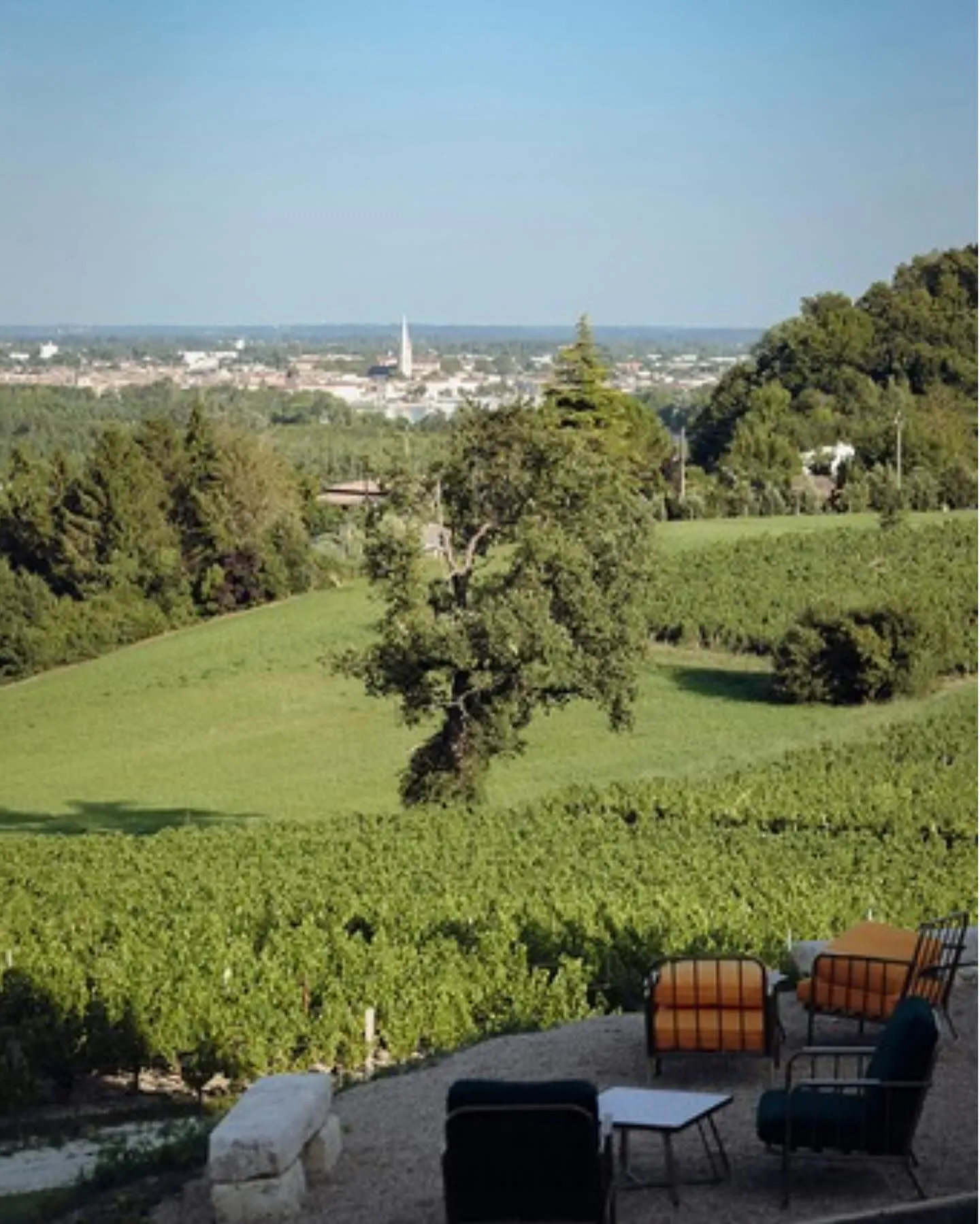 Panoramic view from Château CarlMagnus terrace overlooking Bordeaux vineyards with the city skyline in the background and outdoor seating in the foreground