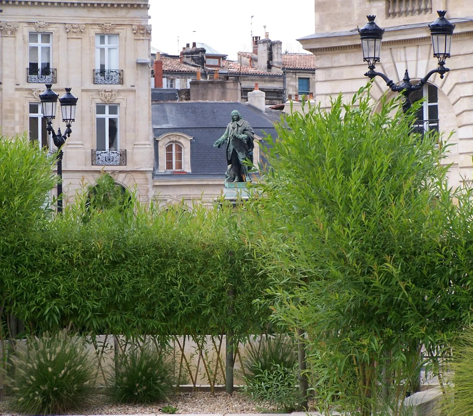 View of Allées de Tourny in Bordeaux featuring a bronze statue in the center, surrounded by lush greenery, classical street lamps, and Haussmann-style buildings in the background