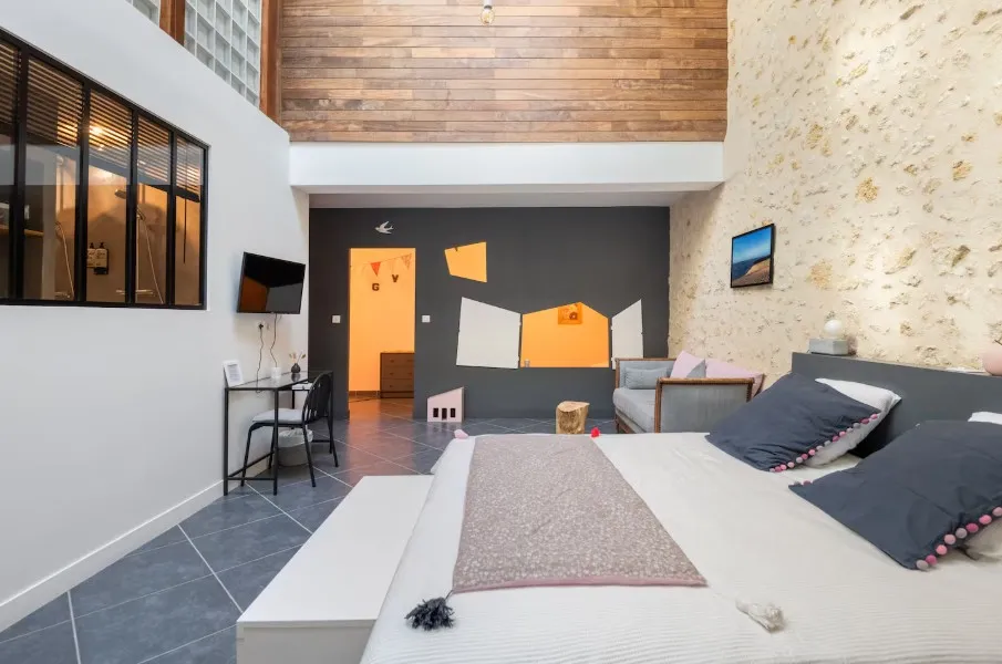 Spacious and modern bedroom at Gatto Verde in Bordeaux featuring a double bed, grey and beige walls, wooden ceiling, contemporary furnishings, and access to a bright communal area
