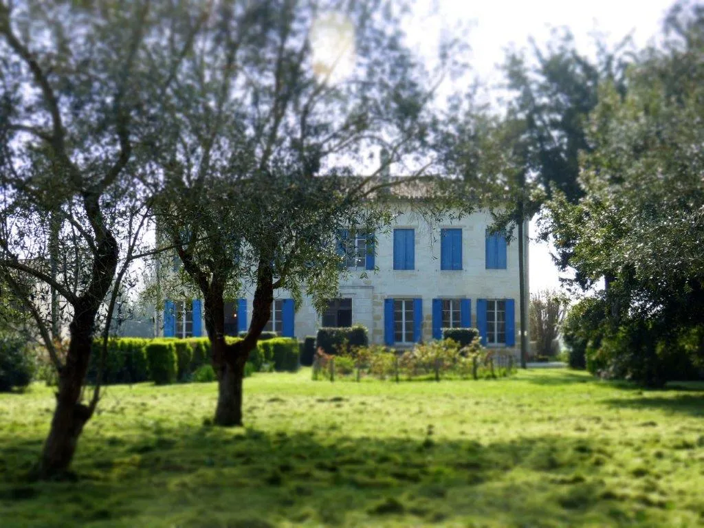 Beau Rivage Estate near Bordeaux, white stone mansion with blue shutters surrounded by olive trees and manicured gardens