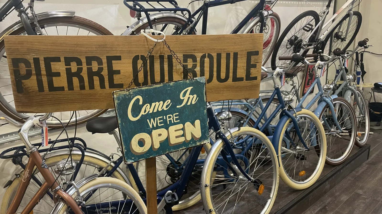 Pierre qui Roule bike rental shop in Bordeaux displaying multiple blue and brown bicycles with an "Come In WE'RE OPEN" sign