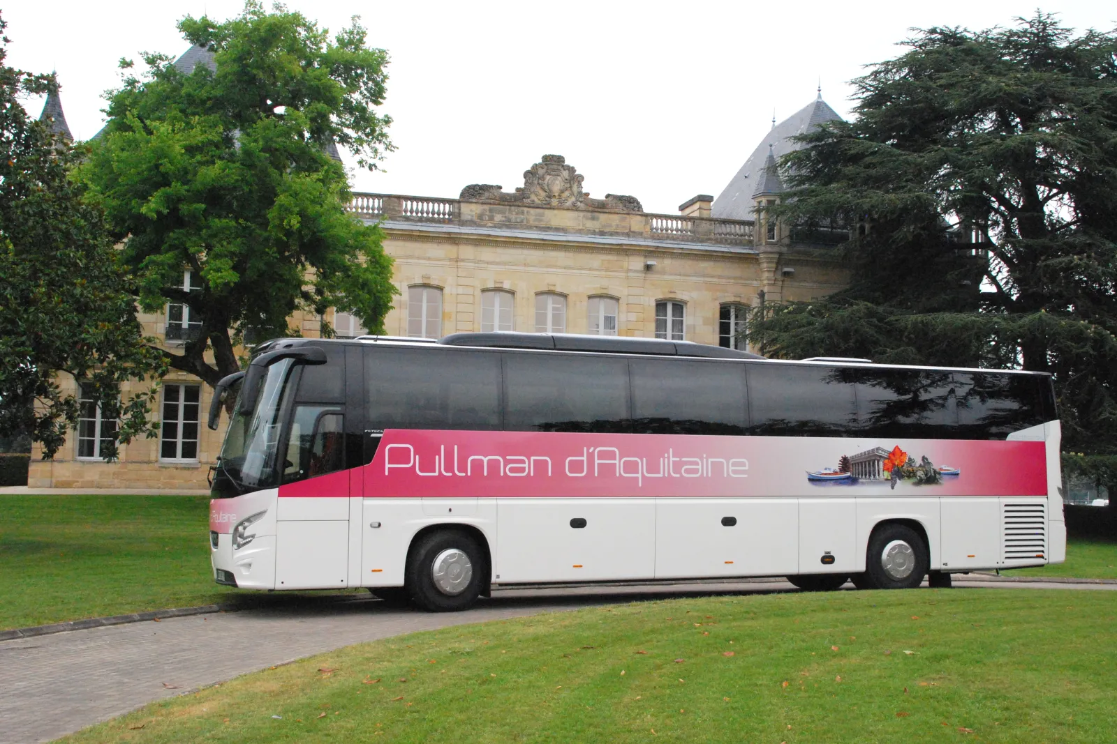 White and pink Pullman d'Aquitaine coach bus parked in front of a historic château in Bordeaux, with lawn and trees in the background