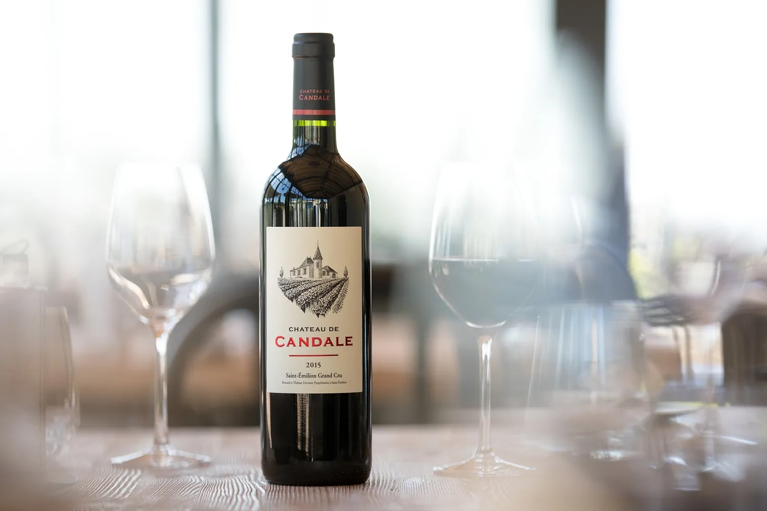 Bottle of Château de Candale 2015 red wine, Saint-Émilion Grand Cru, surrounded by empty wine glasses on a table with blurred background