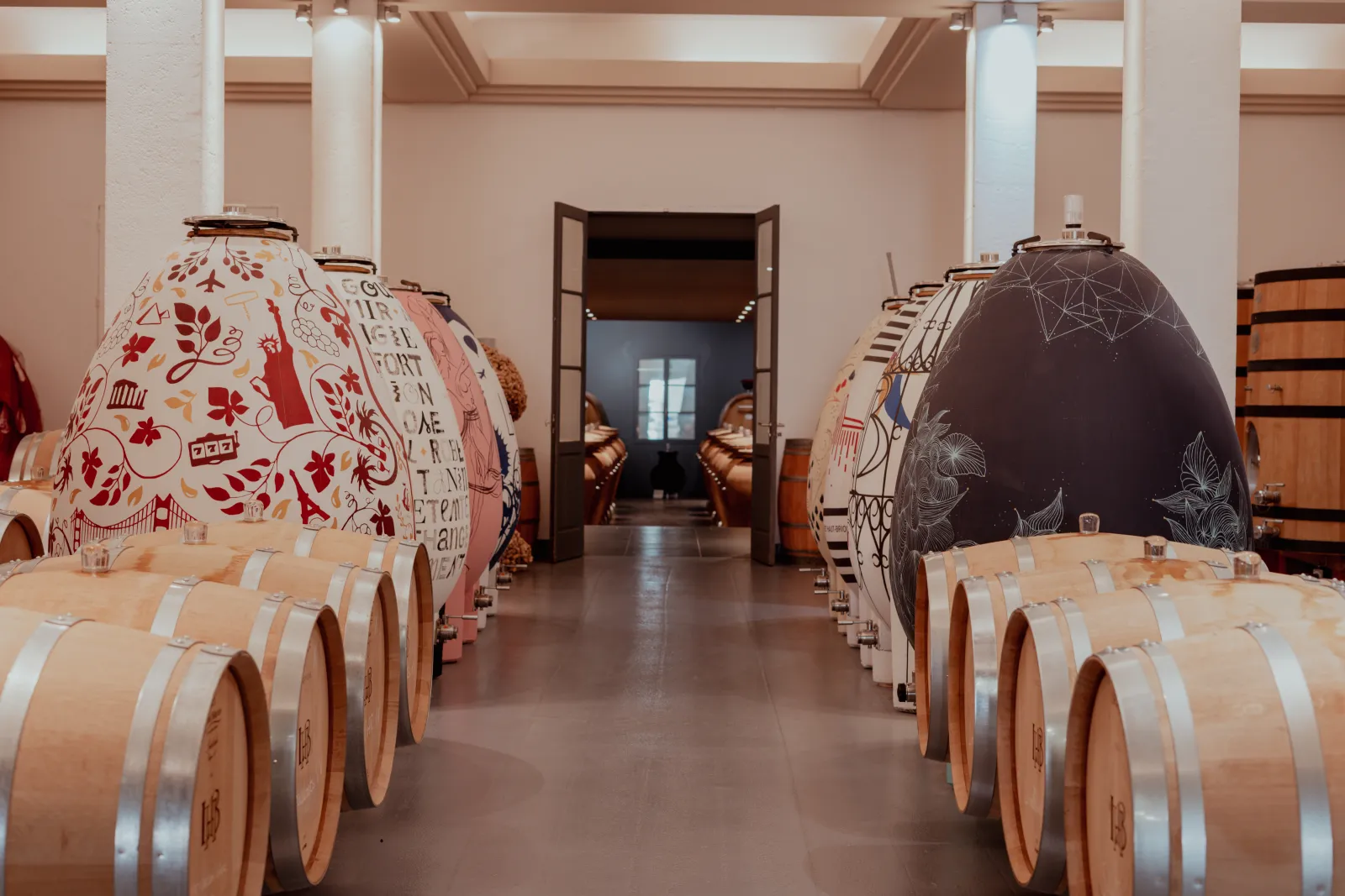 Interior of a wine cellar at Château Larrivet Haut-Brion in Bordeaux, featuring wooden barrels and fermentation tanks decorated with artistic patterns, in a room with white columns.