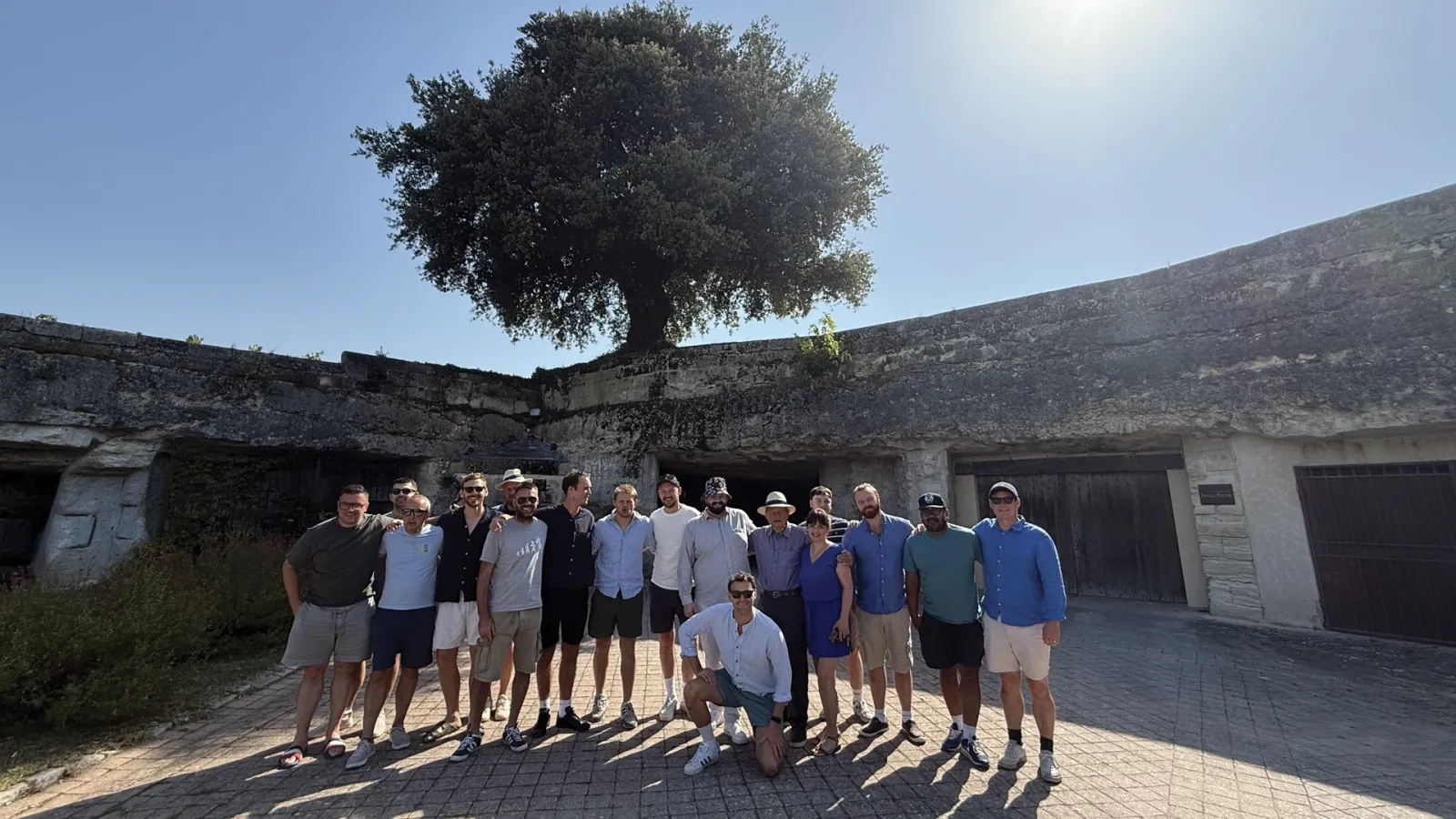 Group of tourists standing in front of ancient ruins with a large tree overhead during a guided tour in Bordeaux.