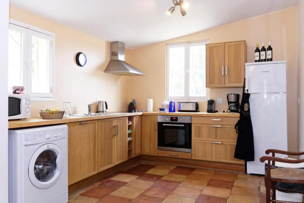 Modern equipped kitchen with wooden cabinets, white appliances, terracotta tiles, and pale peach walls in a Bordeaux property.