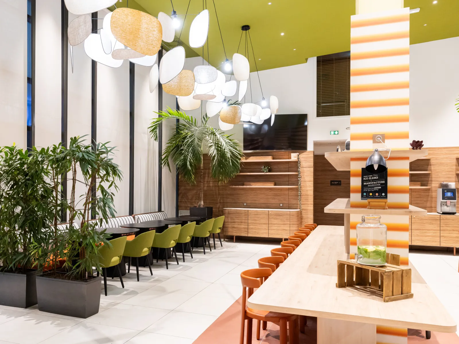 Modern reception area of Adagio Bordeaux Gambetta featuring chartreuse ceiling, white and wooden designer pendant lights, contemporary light wood furniture, yellow-green chairs, green plants and orange accents.