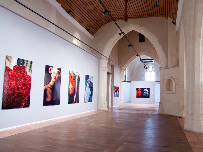 Modern art gallery inside a historic church featuring barrel vaults, wooden ceiling, and colorful photographs displayed on white walls