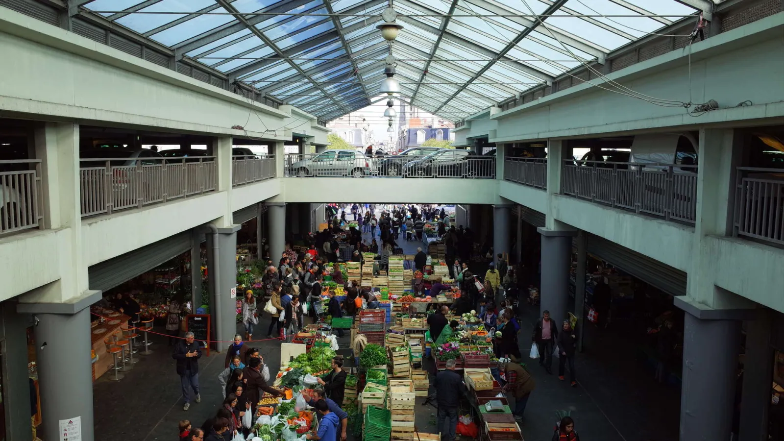 Overhead view of Capucins Market in Bordeaux showing produce stalls, crowds of shoppers, modern architecture with glass roof and green balconies.