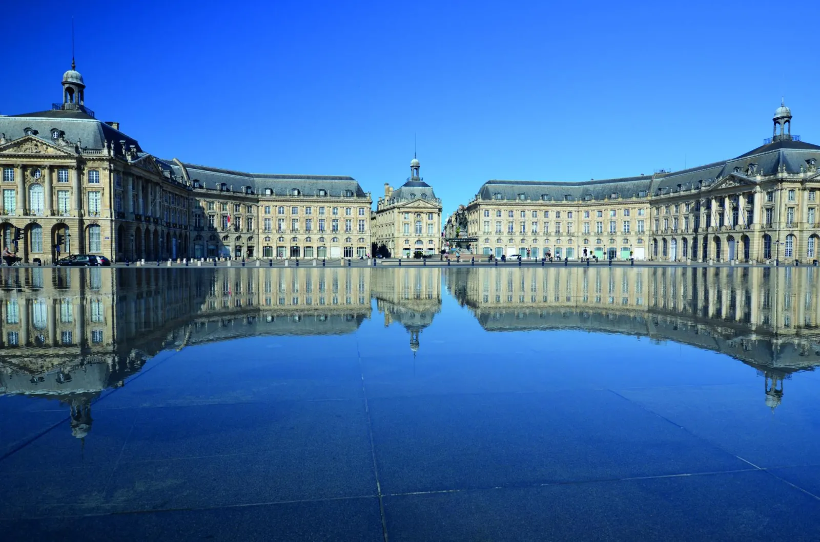 Bordeaux's Place de la Bourse featuring classical golden stone buildings reflected in a still water mirror under clear blue sky
