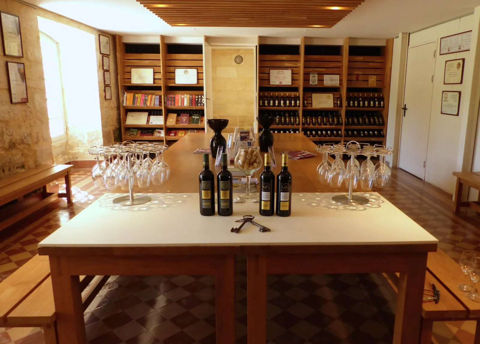Tasting room at Château Sainte Barbe in Bordeaux featuring a central table, wine bottles, wine glasses and wooden storage shelves