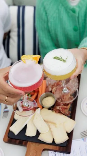 Two elegant cocktails in Bordeaux: a pale pink drink and a creamy white topped with rosemary, served with a cheese and charcuterie board