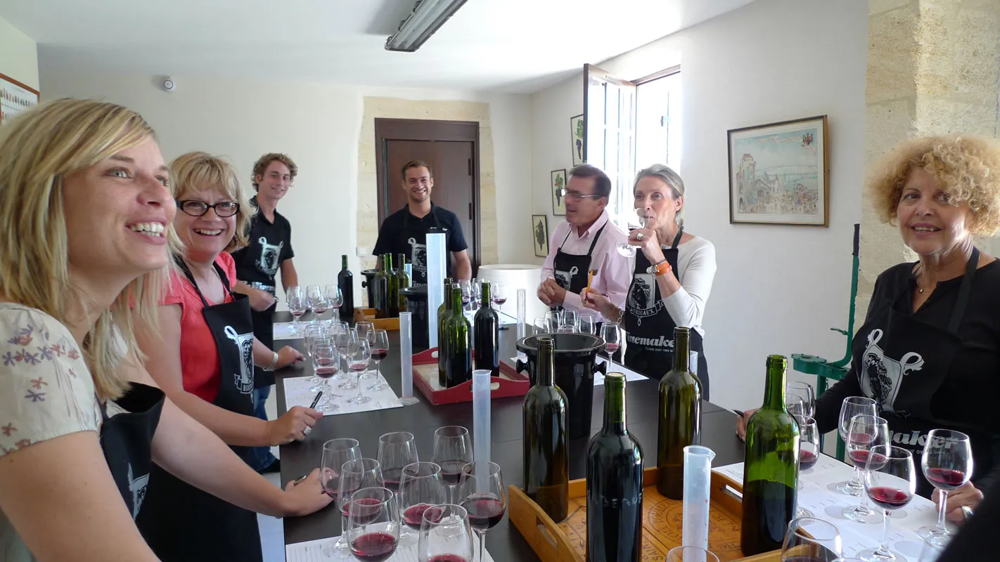 Group of people enjoying a wine tasting in Bordeaux, with glasses of red wine and bottles on the table in a bright room.