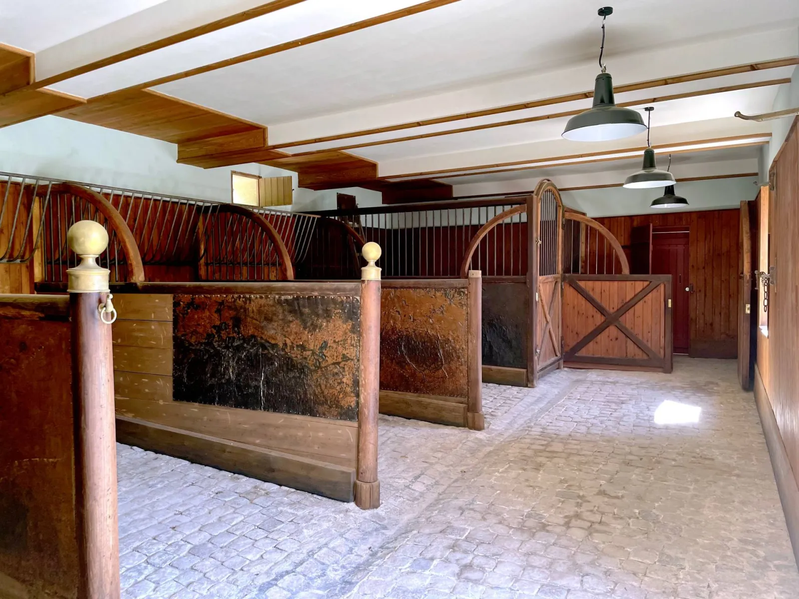 Historic stable at Château de La Brède in Bordeaux featuring wooden horse stalls, exposed beams, and industrial pendant lights
