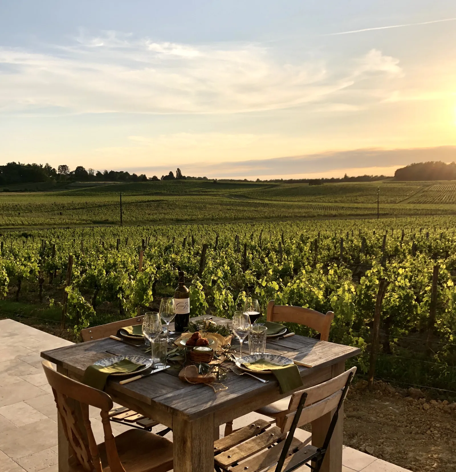 Dining table set on a terrace overlooking Bordeaux vineyards at sunset, with glasses and place settings at Château George 7