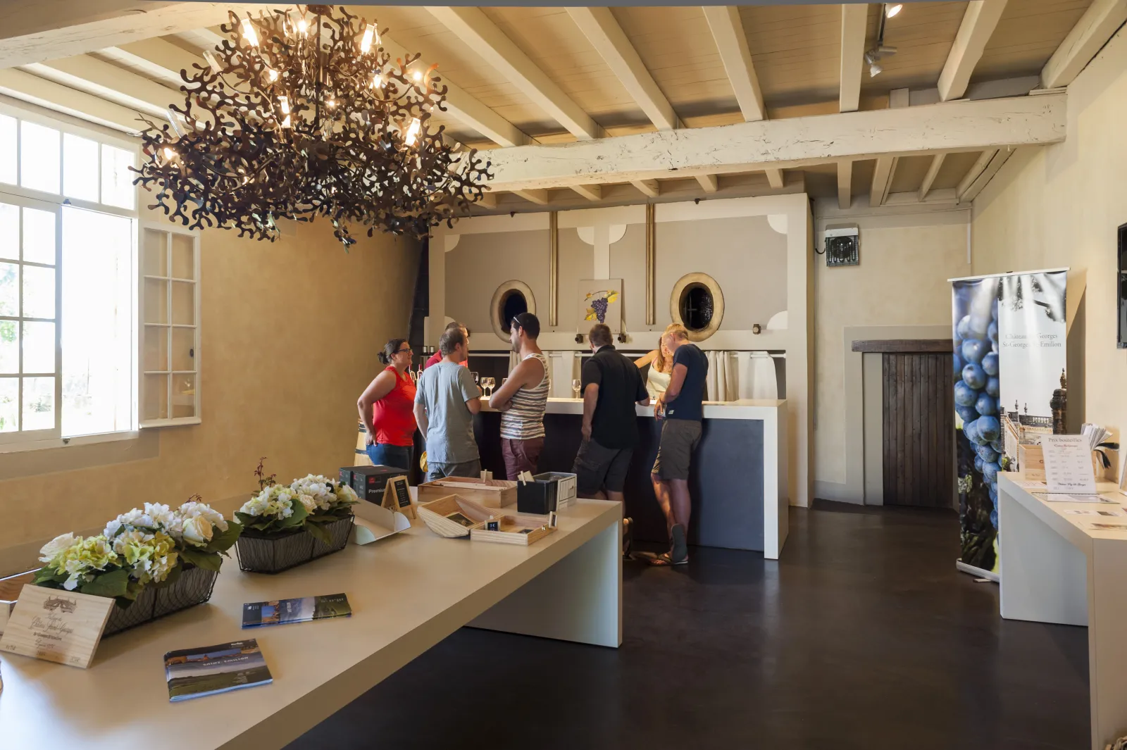 Elegant reception area at Château Saint-Georges in Bordeaux featuring visitors at the counter, sculptural chandelier, exposed beams, and floral arrangements.