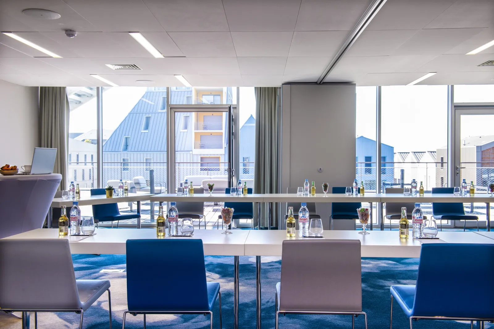 Modern conference room at Radisson Blu Hotel Bordeaux featuring white tables, blue and grey chairs, panoramic city views through floor-to-ceiling windows, and contemporary décor.