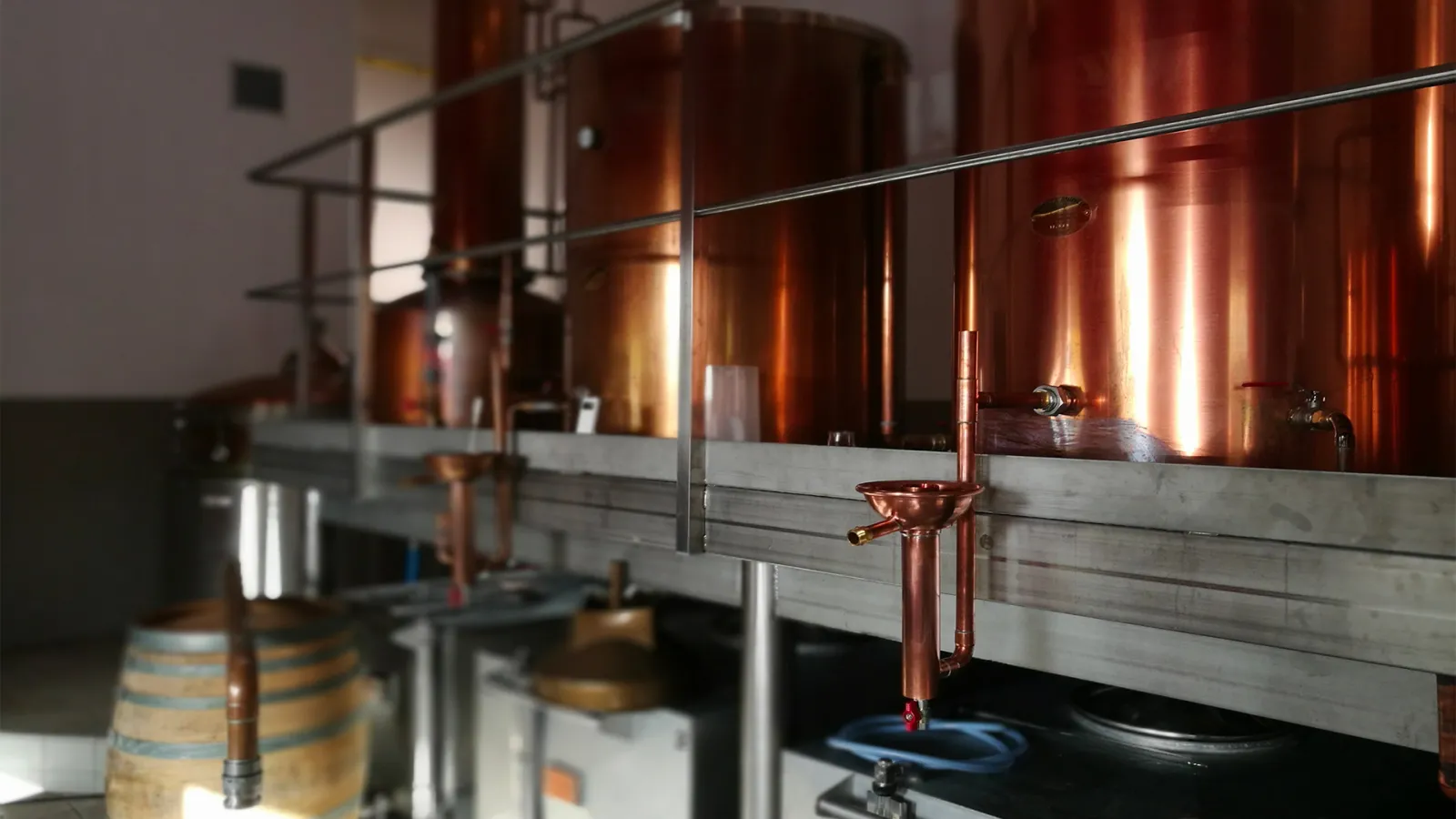 Interior of Moon Harbour distillery in Bordeaux featuring glowing copper stills, copper piping, a metal railing, and a wooden barrel in the foreground.