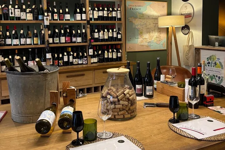 Interior of a Bordeaux wine cellar featuring a tasting counter, wine bottle shelves, a decanter filled with corks, wine glasses, and a French vineyard map displayed on the wall.