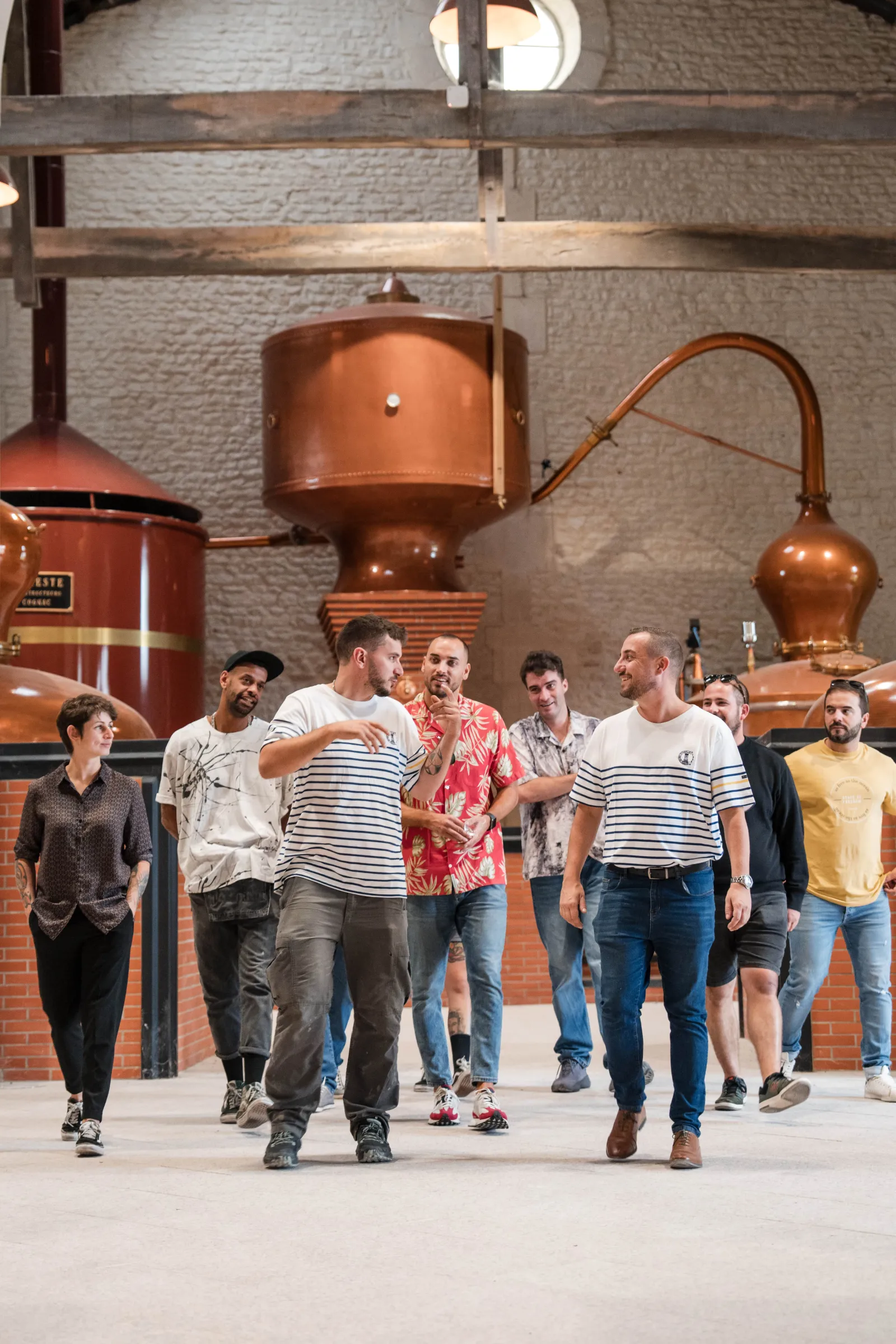 Group of visitors walking through the Citadelle Gin distillery in Bordeaux, with traditional copper stills in the background.