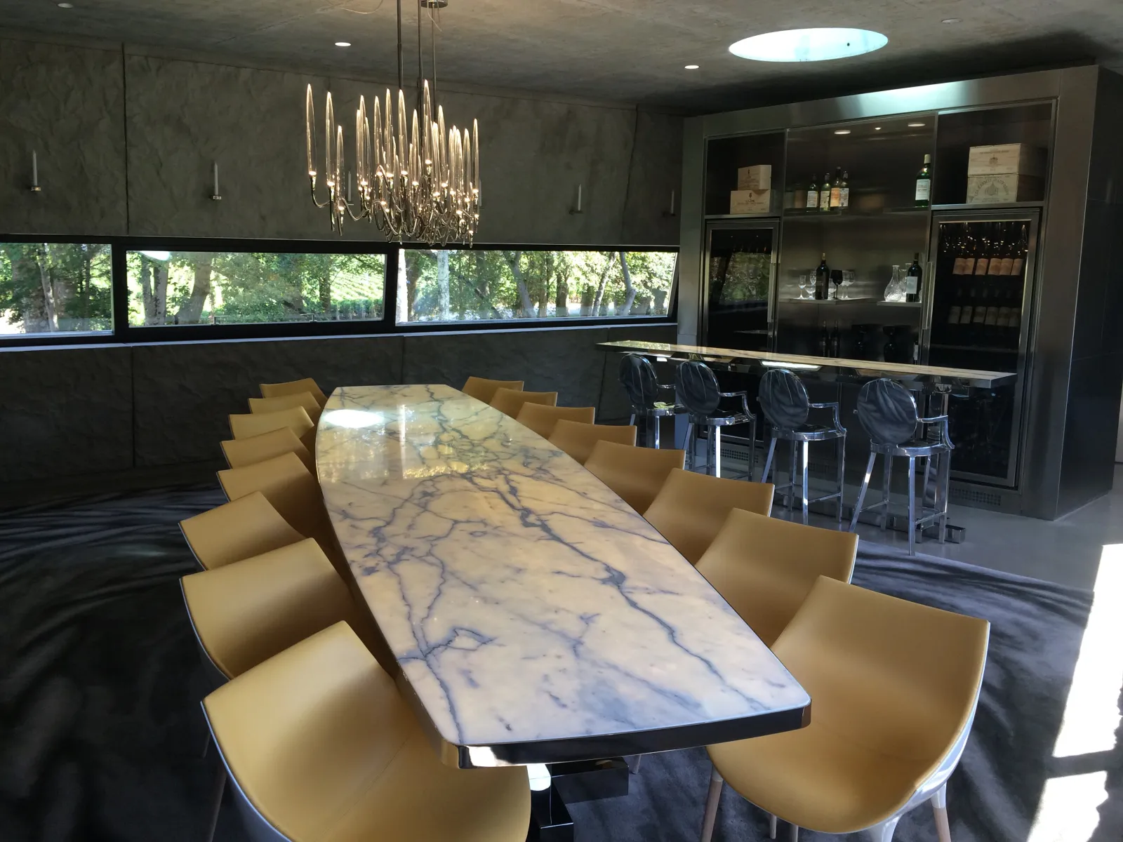 Modern reception hall at Château les Carmes Haut-Brion in Bordeaux featuring a long white marble table with golden yellow chairs, elegant bar in the background, and large windows overlooking the vineyards