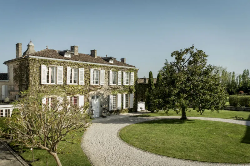 Château Prieuré-Lichine in Bordeaux, classic winery estate featuring white façade, grey shutters, climbing ivy, gravel driveway and landscaped grounds.