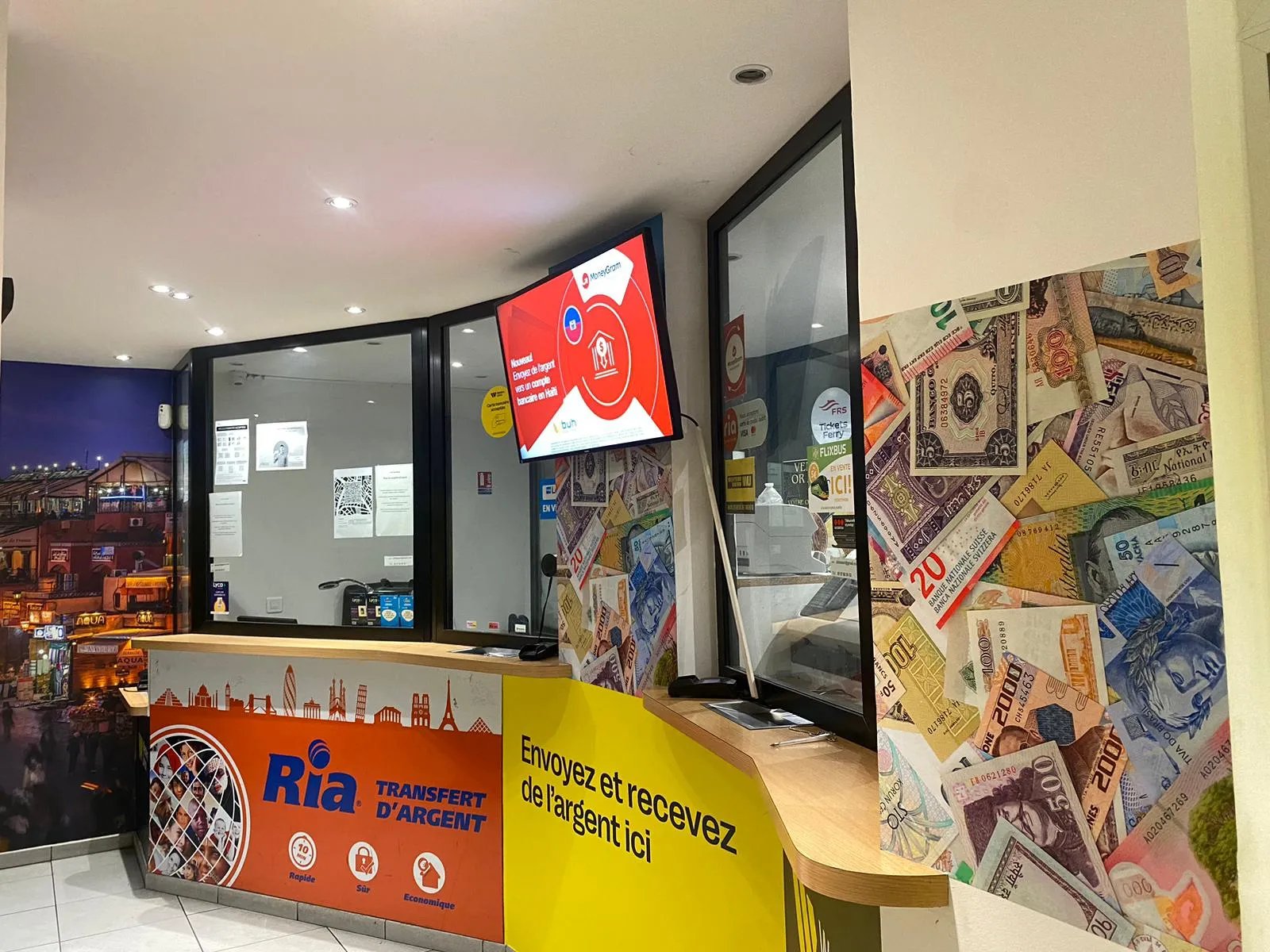 Storefront of Ria Money Transfer exchange office in Bordeaux Gambetta, featuring orange and yellow counter, red digital display, and wall decoration with international banknotes and stamps.