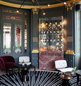 Elegant interior of Grand Barrail restaurant in Bordeaux featuring dark blue walls, gold lighting fixtures, burgundy velvet armchairs, illuminated bar with geometric floor patterns