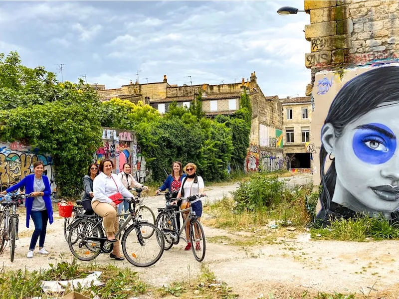 Group of tourists cycling through an abandoned urban area in Bordeaux, featuring historic ruined buildings and colorful street art on the walls