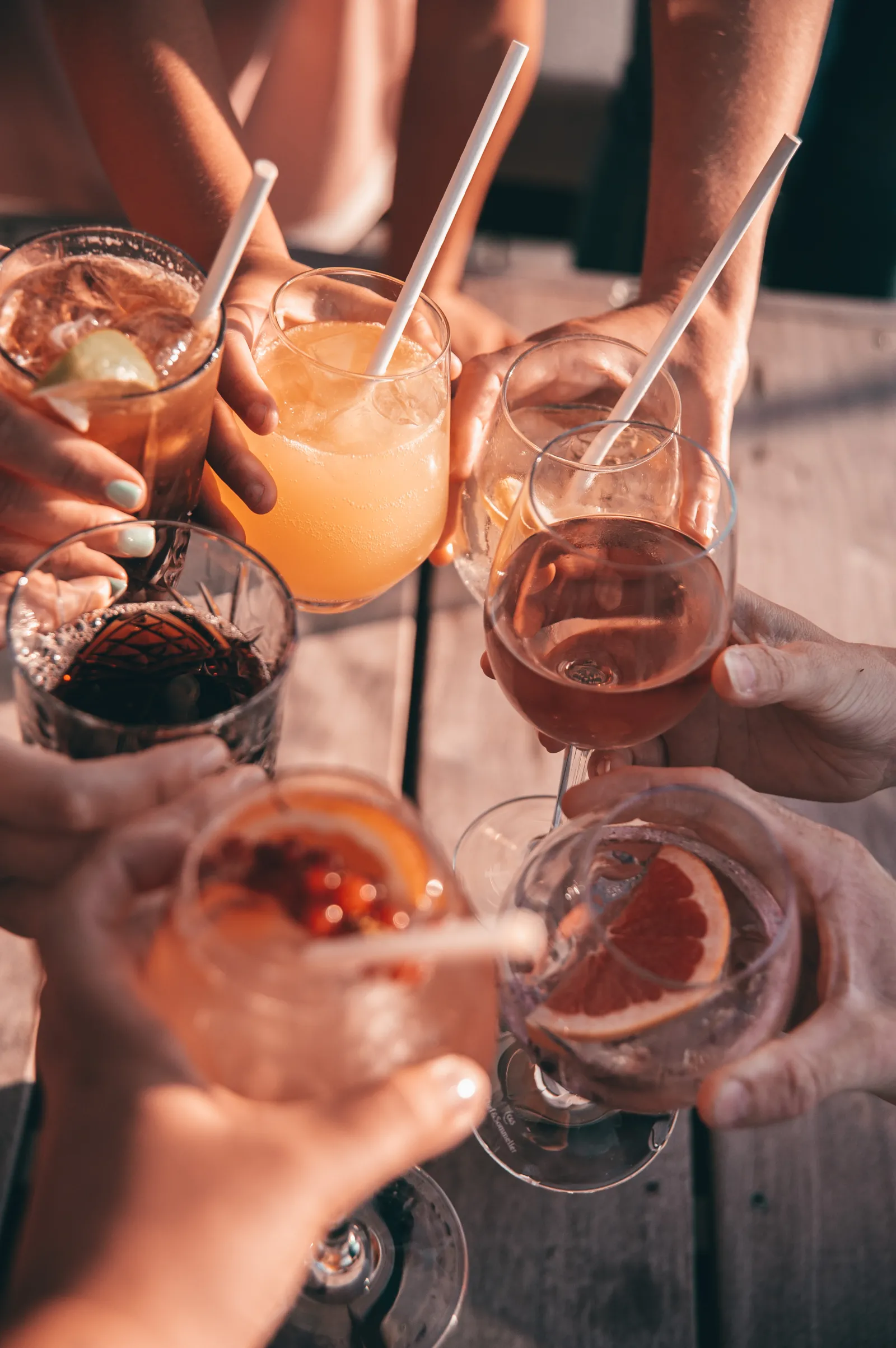 Group of people holding colorful cocktails and beverages during a sunny toast gathering in Bordeaux