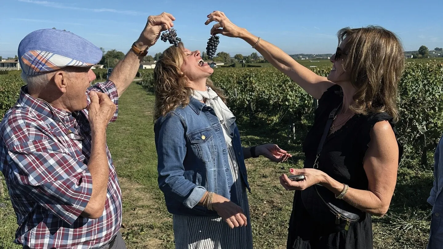 Three people tasting black grapes in a Bordeaux vineyard in Aquitaine, under clear blue sky.